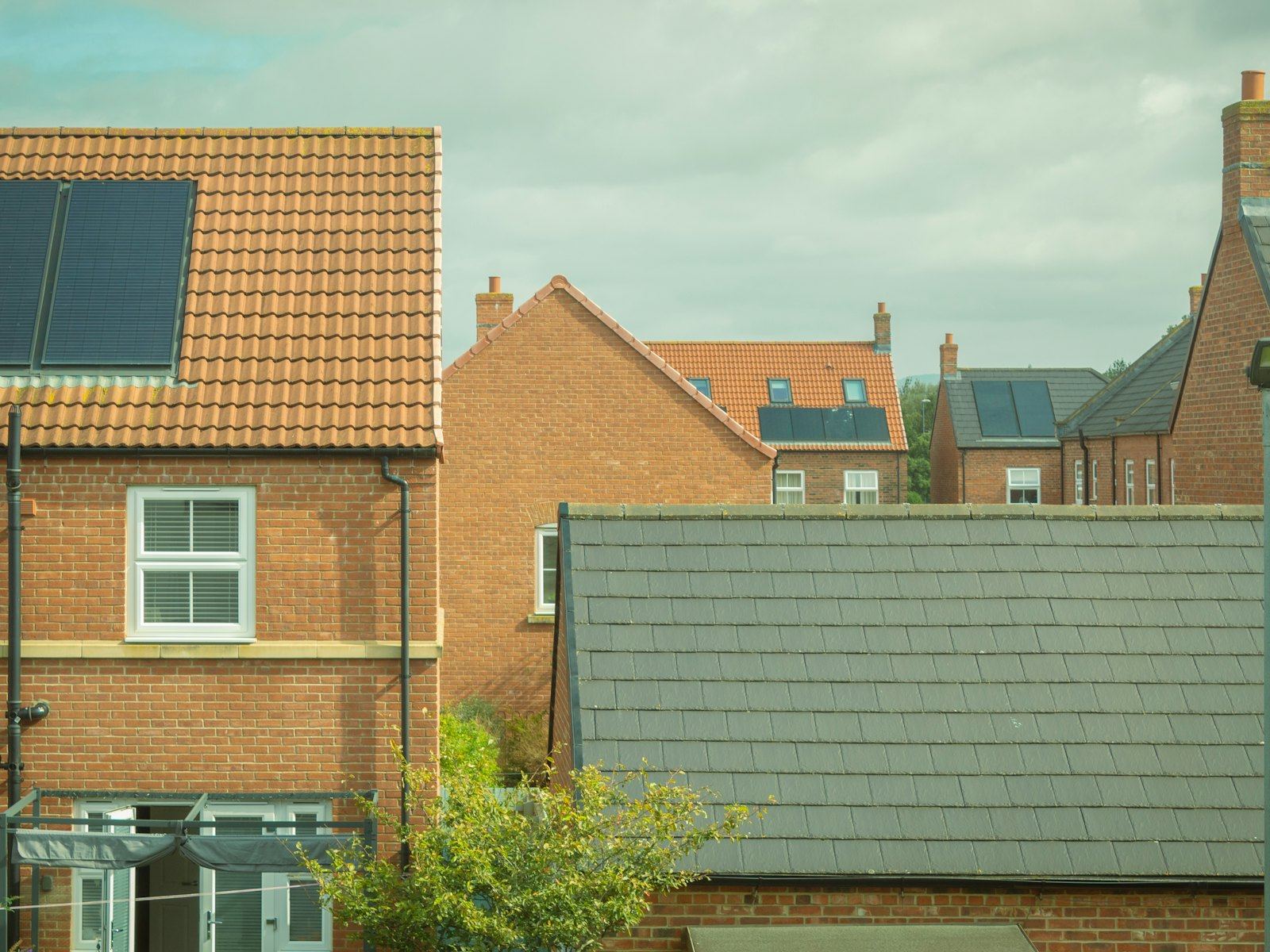 Rooftops of modern brick houses with solar panels under a cloudy sky.