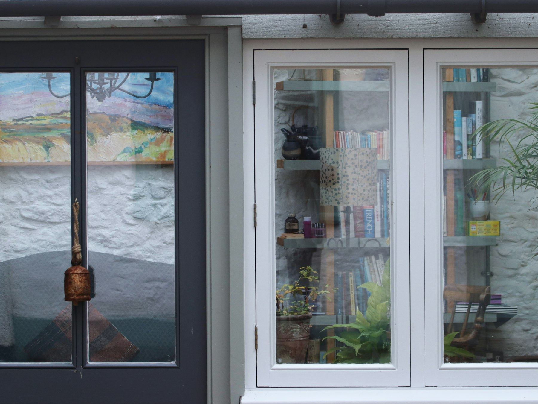 Dark door and white window of a cosy garden room filled with books and plants.