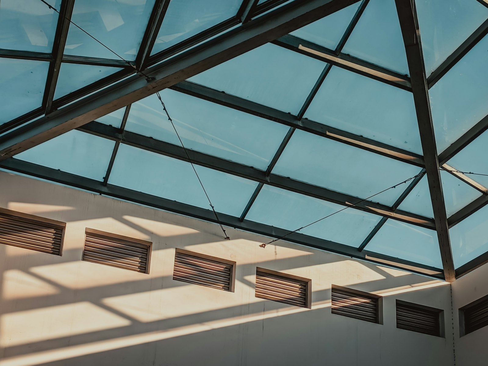 Interior view of a glass roof with steel beams and sunlight.