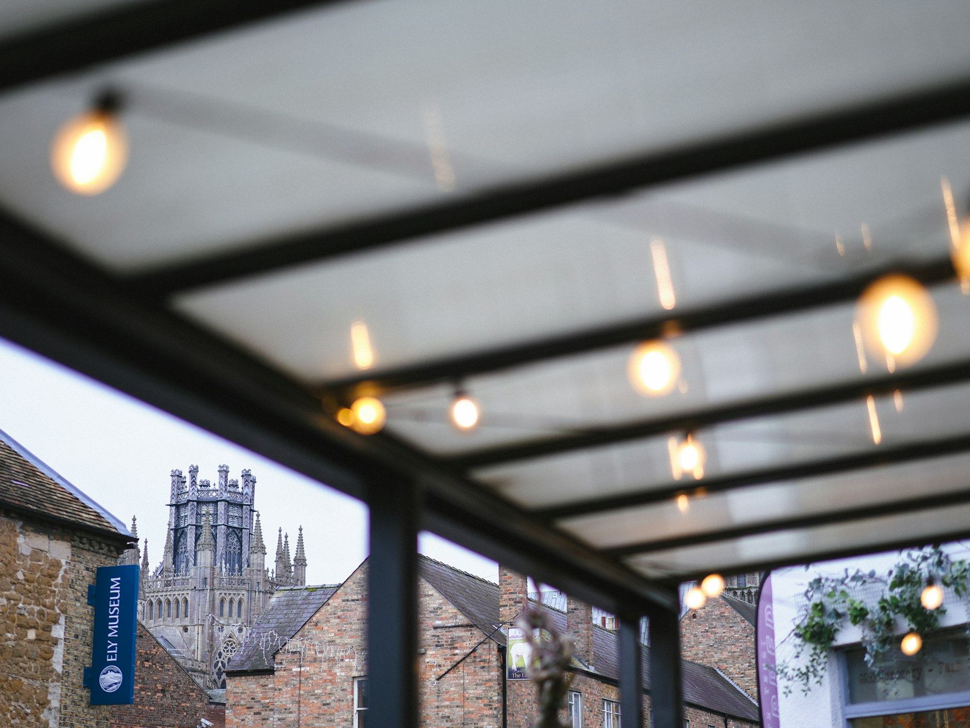 People walking under a lit canopy roof near an old cathedral tower.
