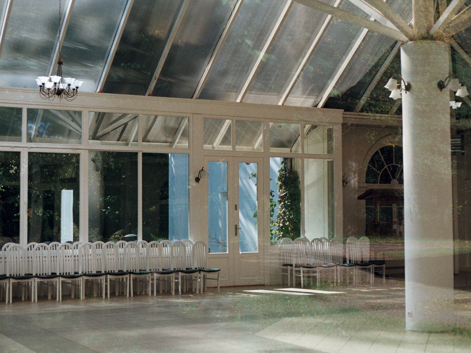 Large conservatory hall with rows of white chairs and a glass roof.