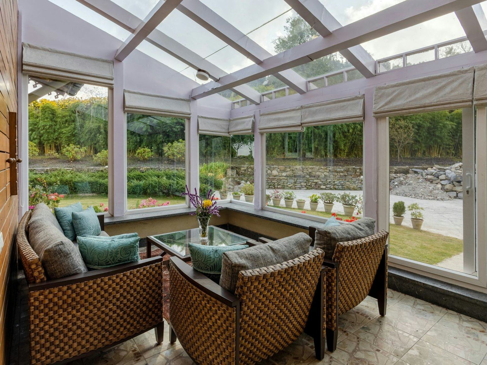 Sunlit conservatory with wicker armchairs overlooking a garden.