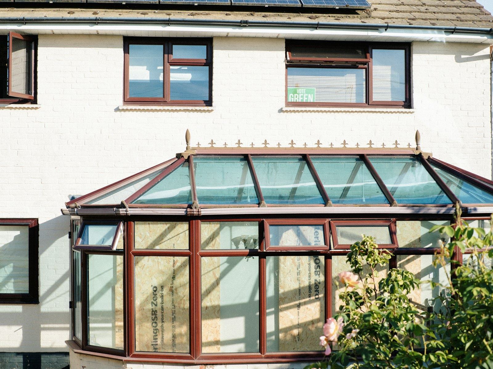 White painted 1930s semi-detached house with a brown conservatory and solar panels.